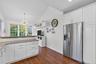 Kitchen featuring white cabinets, stainless steel refrigerator with ice dispenser, lofted ceiling, dark wood-type flooring, and light stone counters
