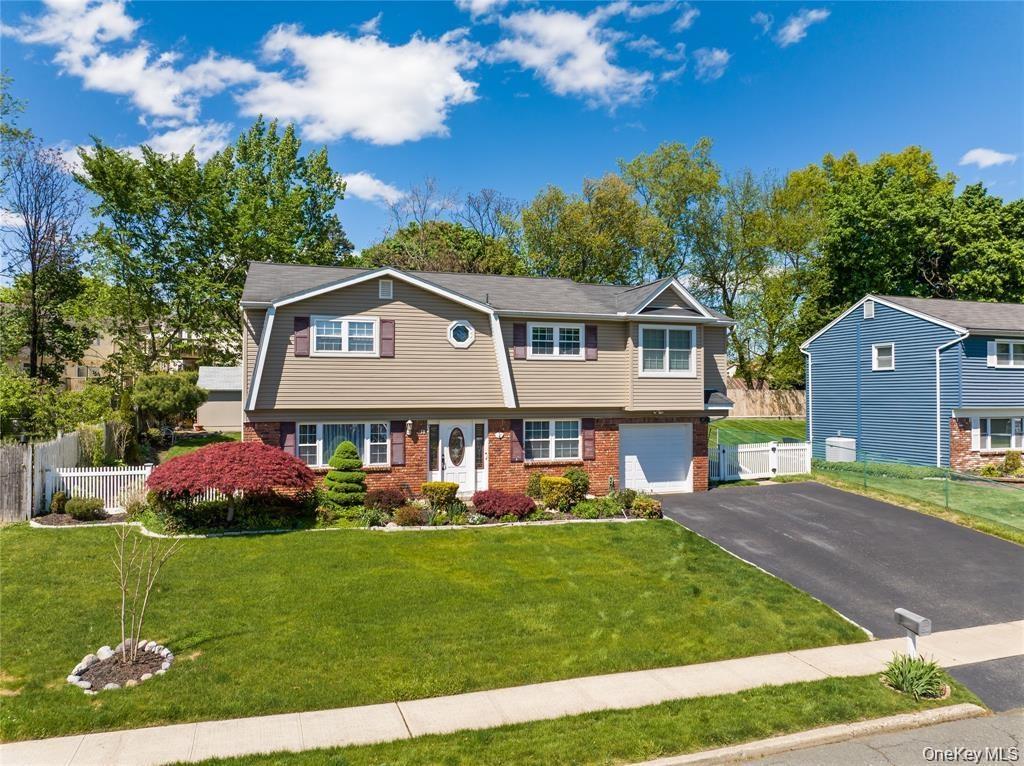 Split-level residence featuring a brick and siding facade, a manicured front lawn, a paved driveway, an attached garage, and mature landscaping