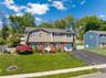 Split-level residence featuring a brick and siding facade, a manicured front lawn, a paved driveway, an attached garage, and mature landscaping