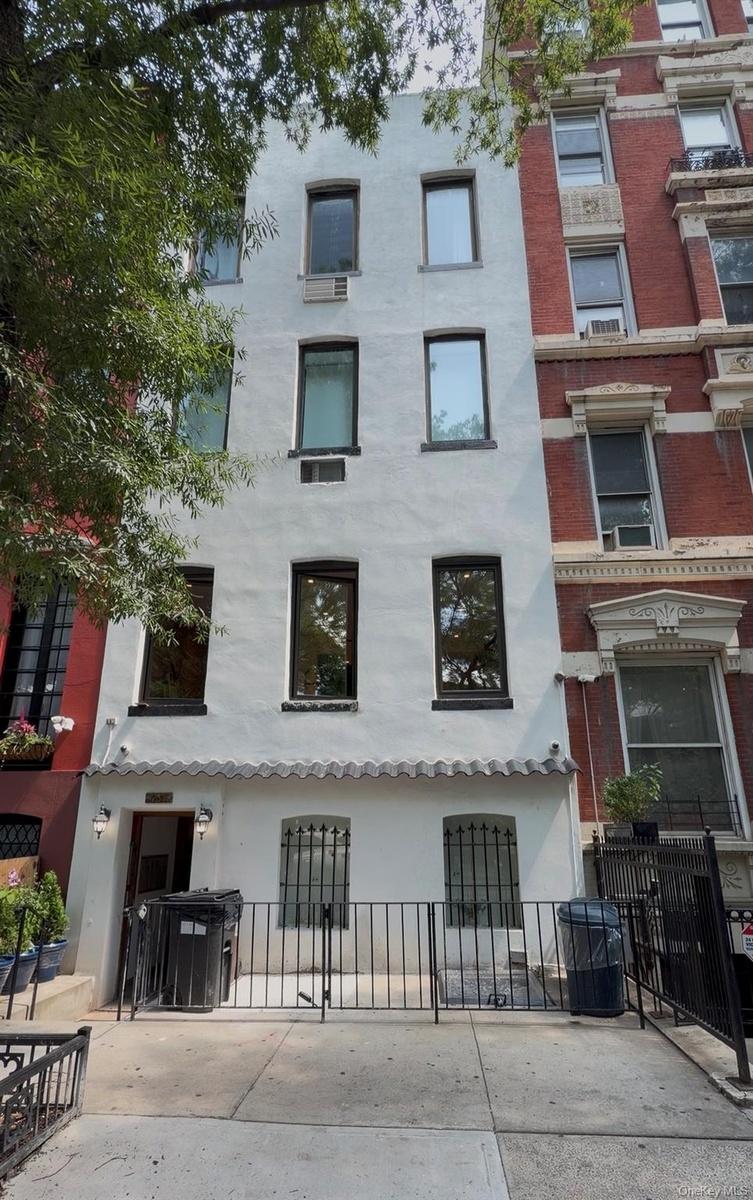 White stucco facade with multiple windows, a ground-level wrought iron fence, and a short entry awning
