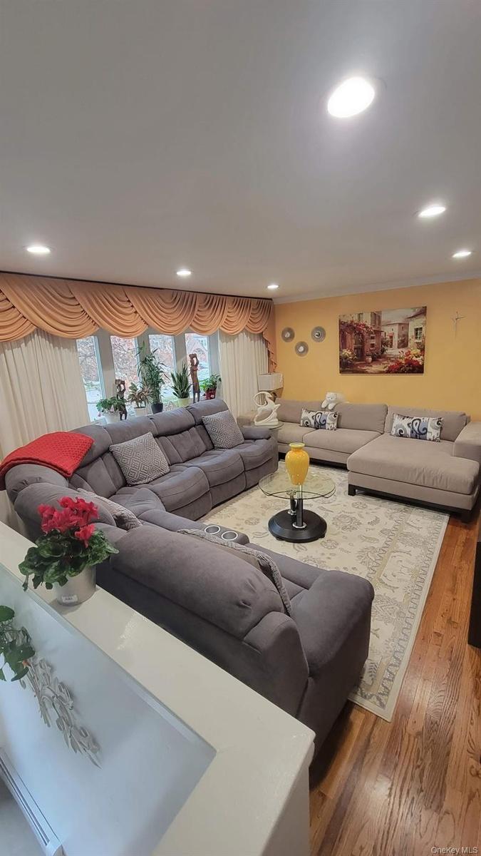 Spacious living area featuring wood-finish flooring, recessed ceiling lights, and a large window with draped valances