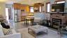 Open-concept living space featuring a brick fireplace with a dark mantel, wood-finish flooring, and natural wood window trim