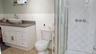 Bathroom featuring a walk-in shower with glass enclosure, white tile walls, a white vanity with vessel sink, and a toilet