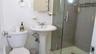 Bathroom featuring a pedestal sink with chrome faucet, toilet, and a glass-enclosed shower with gray tiled walls