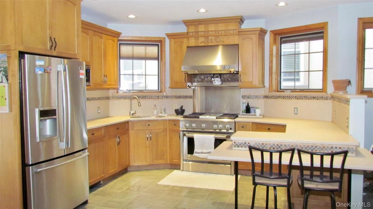 Full kitchen featuring stainless steel appliances, custom wood cabinetry, extensive countertop space, recessed lighting, and tile flooring