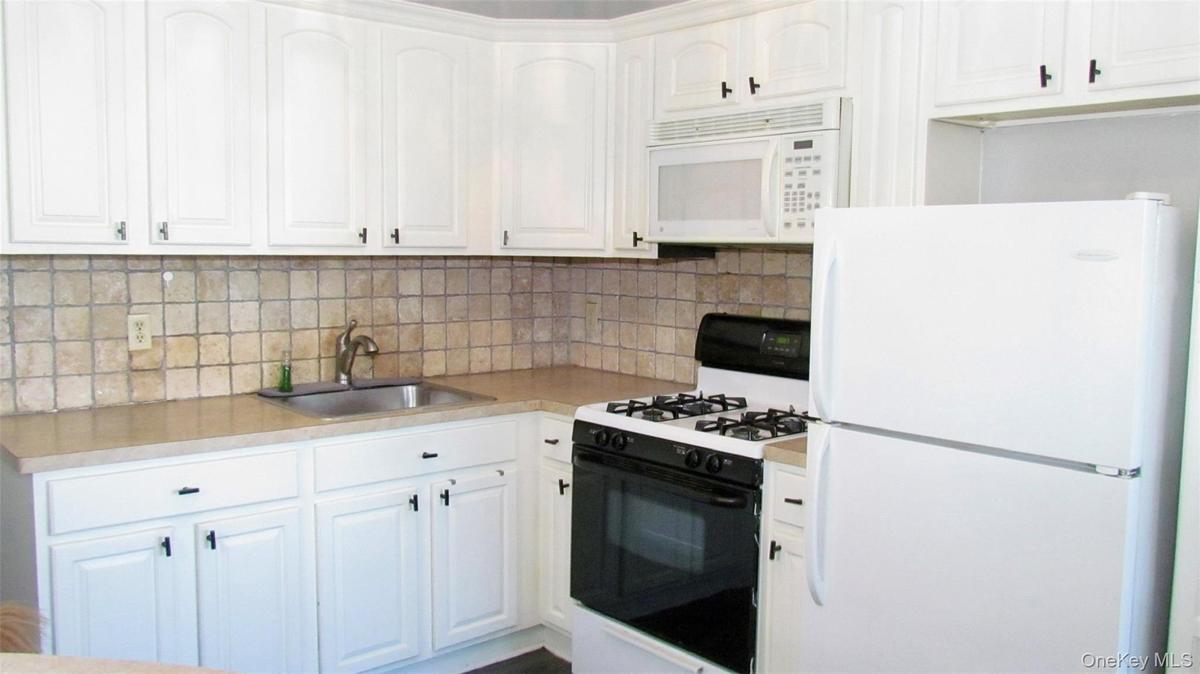 Kitchen featuring white cabinetry, light-toned countertops, a square tile backsplash, and a stainless steel sink