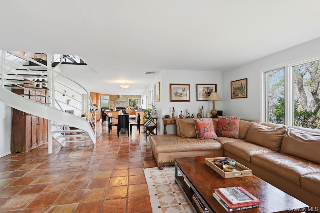 Open-concept living area featuring terracotta tile flooring, a white spiral staircase, and large windows