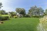 Expansive manicured lawn featuring a white gazebo with drapes, surrounded by mature trees and varied landscaping