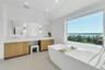 Freestanding soaking tub positioned before an expansive window overlooking a body of water and treeline