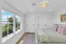Light-filled bedroom featuring a multi-pane window overlooking a body of water and lush greenery, wood-finish flooring, two sliding closet doors with 