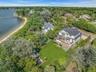 Modern coastal home with multiple outdoor decks, a manicured lawn, and mature trees, featuring a private sandy beach and a long dock extending into th