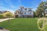 Custom coastal residence featuring board and batten siding, natural wood shingle accents, multiple balconies with black railings, and an expansive fro