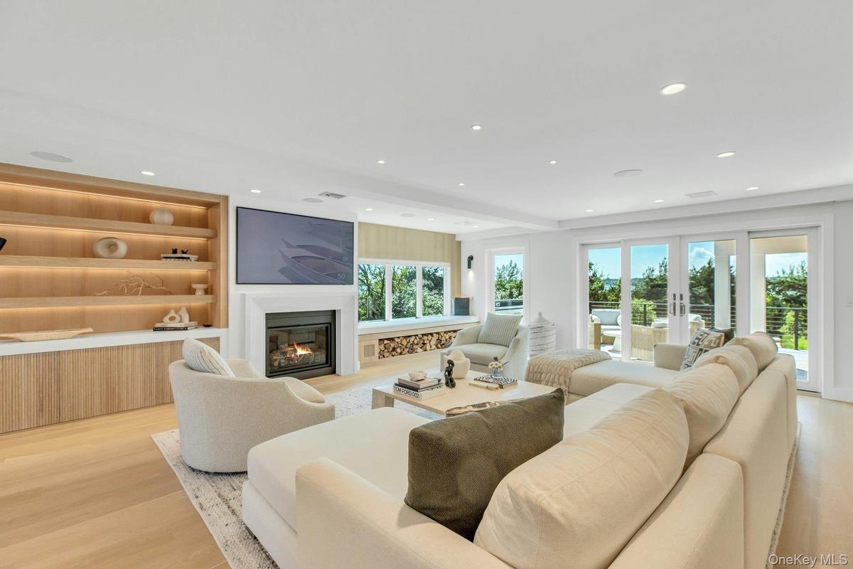 Spacious living area featuring light wood-finish flooring, recessed lighting, and a built-in entertainment center with open shelving and lower cabinet