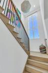 Hardwood staircase with black metal balusters and a wood-finish handrail, complemented by a tall, multi-pane window and a contemporary pendant light f