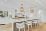 Spacious kitchen featuring an oversized island with countertop seating, light wood-finish flooring, white cabinetry with gold-tone hardware, and integ