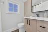 Modern bathroom featuring a wood-finish vanity with matte black hardware, white countertop, rectangular undermount sink, and a black-framed mirror