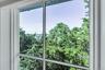 White-framed window with multiple panes overlooking abundant green trees and a body of water