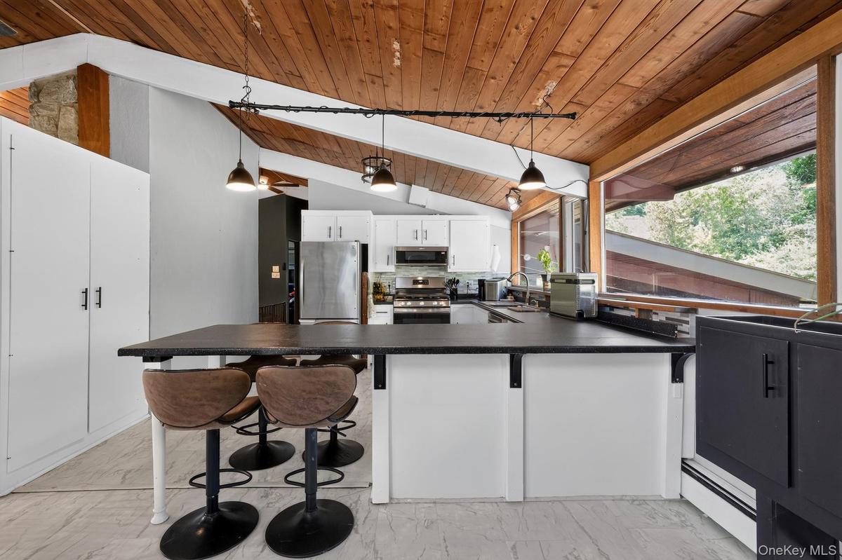 Kitchen featuring an angled wood-panel ceiling, white cabinetry with stainless steel appliances, and a large central island with a dark countertop