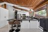 Kitchen featuring an angled wood-panel ceiling, white cabinetry with stainless steel appliances, and a large central island with a dark countertop