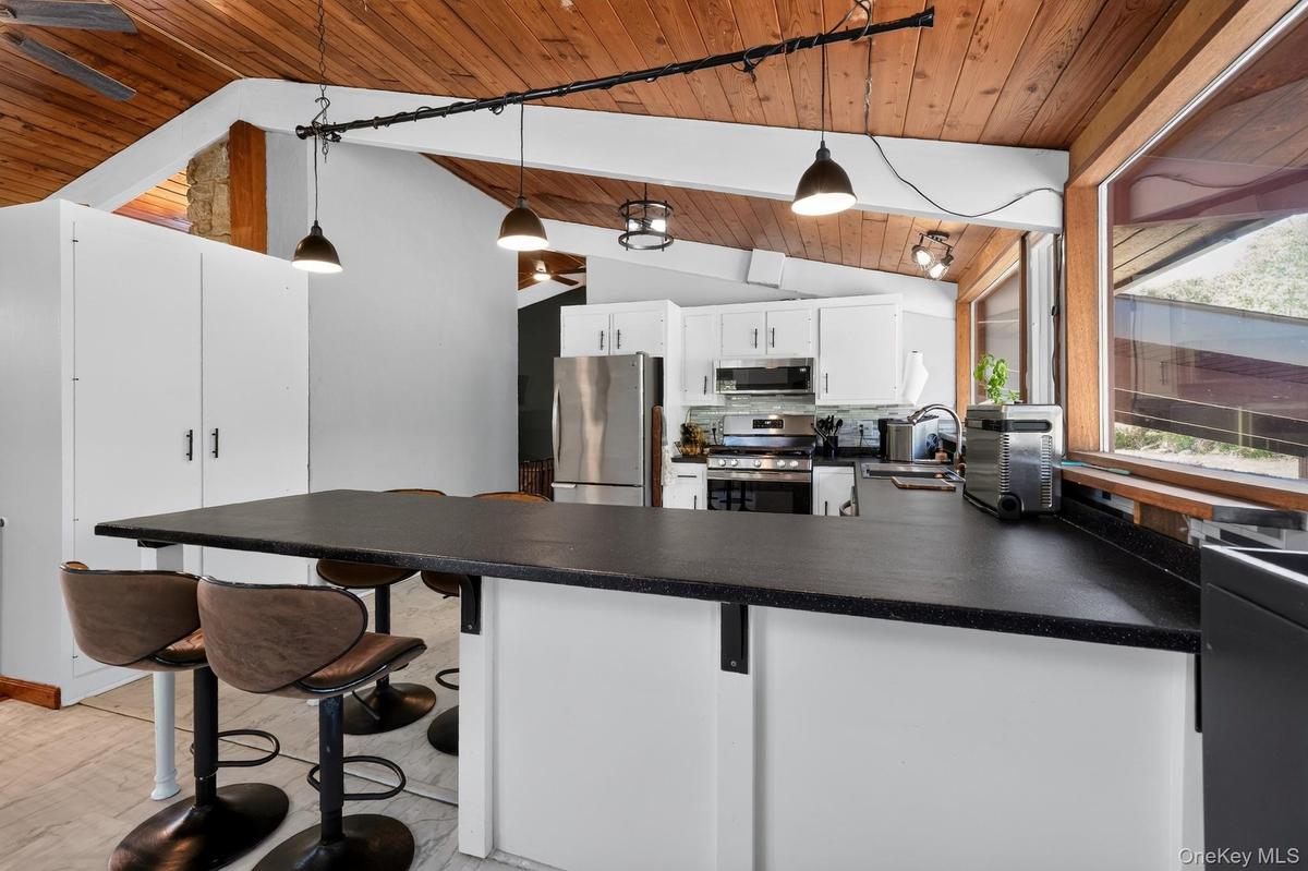 Kitchen featuring a long breakfast bar with a solid surface countertop, white cabinetry, stainless steel appliances, and a wood-paneled vaulted ceilin