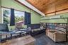 Vaulted wood-paneled ceiling with exposed beams, large picture window with outdoor scenery, full-wall built-in shelving, slate-look flooring, and a wa