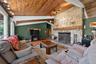 Living area featuring a stone fireplace with a substantial timber mantel, vaulted wood-paneled ceilings, hardwood-style flooring, track lighting, and 