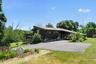 Contemporary architecture featuring a dark brown exterior, expansive asphalt driveway, and an elevated deck with wood railing