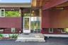 Modern exterior with rich maroon siding, prominent glass entry, and multiple large windows