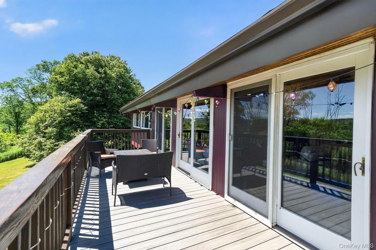 Spacious outdoor deck featuring wood-finish flooring, a full-height wood railing, and multiple glass sliding doors