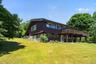 Multi-level exterior with dark siding and white trim, featuring a raised wooden deck, a lower patio, and extensive green lawn space