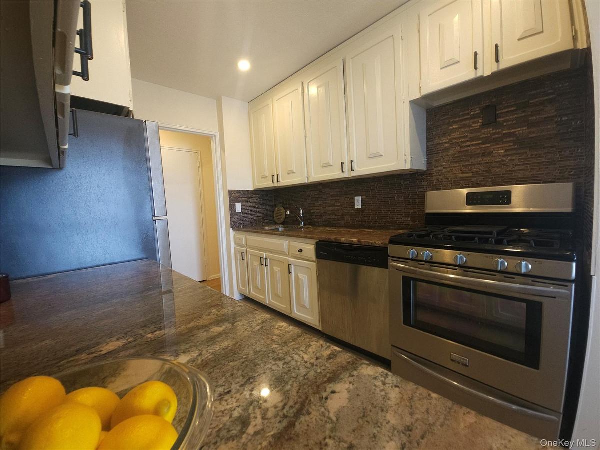 Kitchen featuring granite countertops, a tile backsplash, white cabinetry, and stainless steel appliances