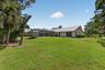 Rear exterior featuring a metal roof, screened lanai, sliding glass doors, and mature landscaping