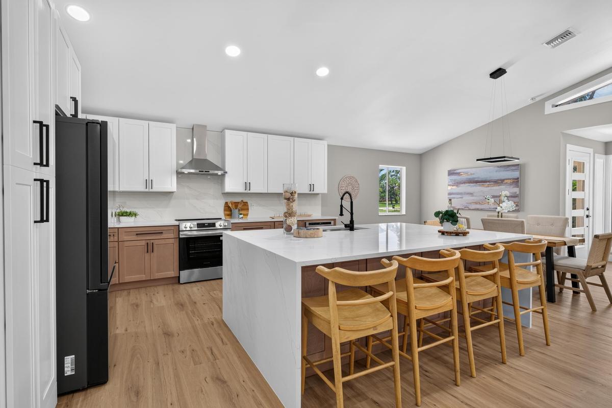 Modern kitchen featuring a waterfall island with a light-toned countertop, two-tone cabinetry, stainless steel appliances, wood-finish flooring, and v