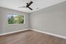 Neutral-toned room featuring a large window, wood-finish flooring, a ceiling fan with integrated lighting, and white baseboards