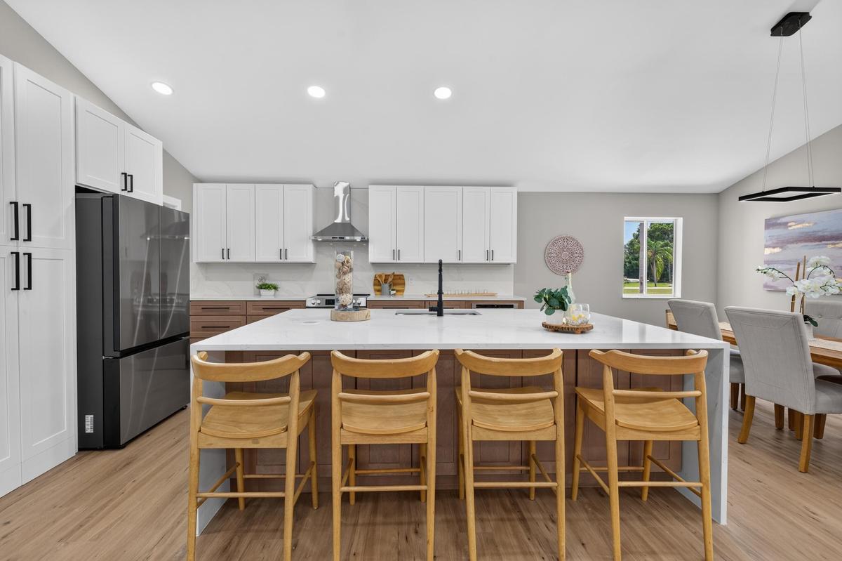 Modern kitchen featuring a large central island with seating, stone countertops, two-tone cabinetry, stainless steel appliances, and wood-finish floor