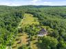 A breathtaking aerial perspective reveals the property’s pristine acreage, beautifully maintained landscaping, open level lawns, and mature wooded are