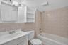 Full bathroom featuring a single vanity, a toilet, a tub with a shower head, and tiled walls