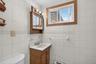 Bathroom featuring white square wall tiles with a decorative border, a wood-finish vanity with an integrated sink, and a matching wood-finish medicine