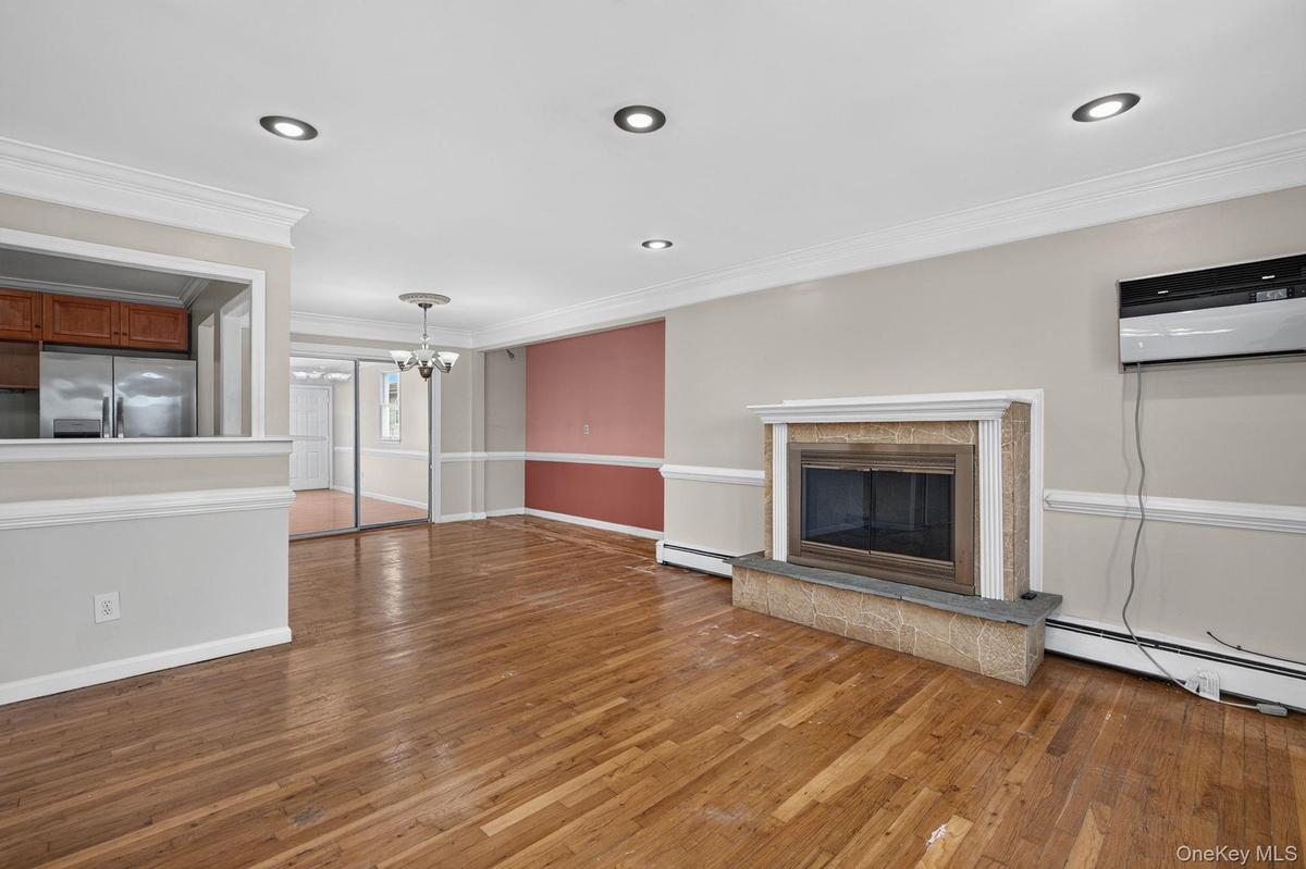Living area featuring wood-finish flooring, a fireplace with a stone surround and hearth, recessed lighting, and crown molding