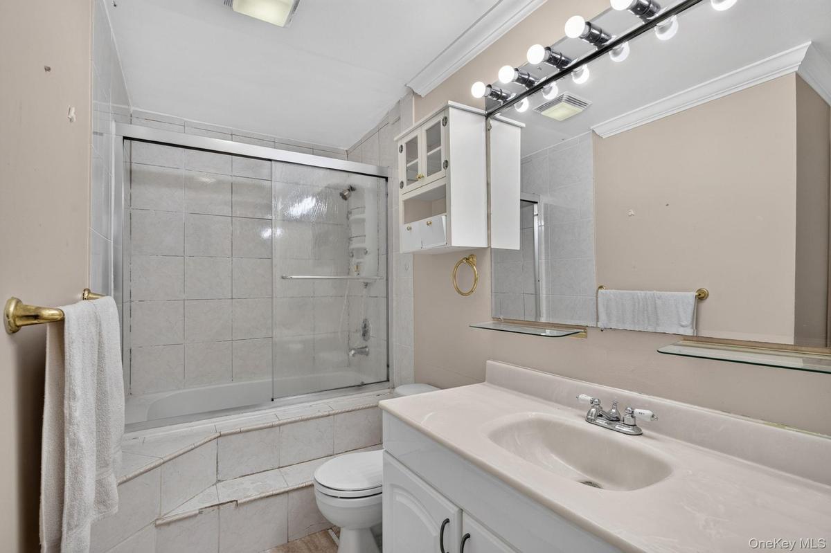 2nd Floor Bathroom featuring a white vanity with integrated sink, a mirrored wall with strip lighting, built-in wall cabinets, and a bathtub with slid