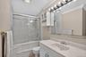 2nd Floor Bathroom featuring a white vanity with integrated sink, a mirrored wall with strip lighting, built-in wall cabinets, and a bathtub with slid