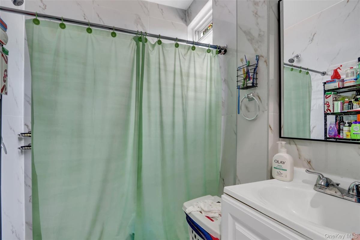 Bathroom featuring white marble-look wall tiles, a white vanity with a ceramic sink, a rectangular framed mirror, and a window providing natural light