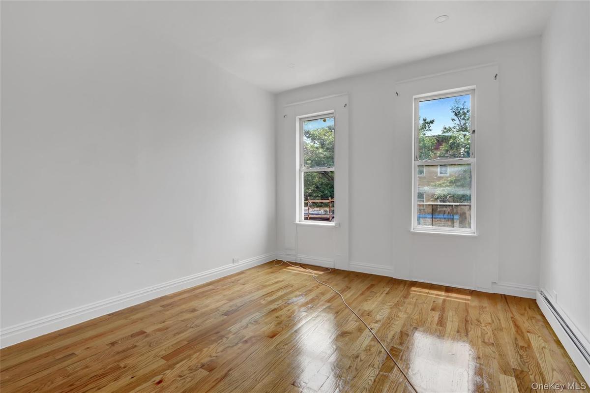 Room featuring two large windows, wood-finish flooring, white baseboards, and white painted walls