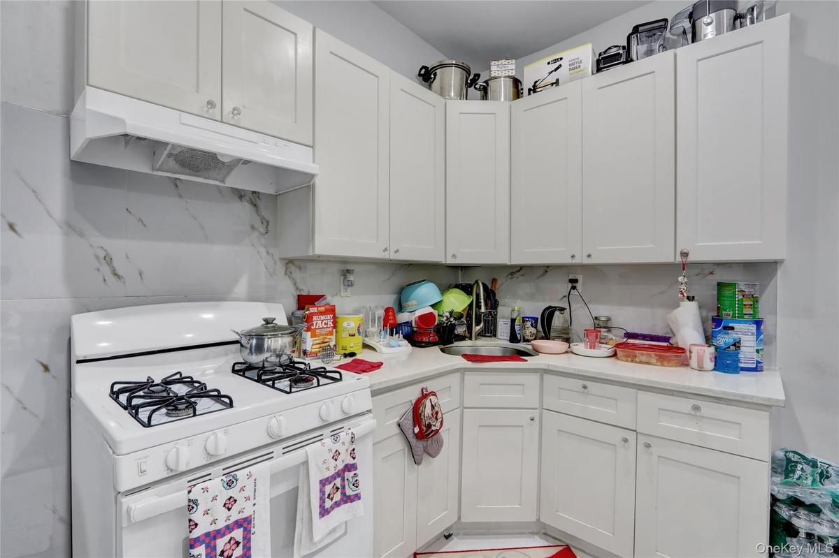 Kitchen featuring white flat-panel cabinetry, white countertops, a white gas range with four burners, a white range hood, and a white and gray veined 