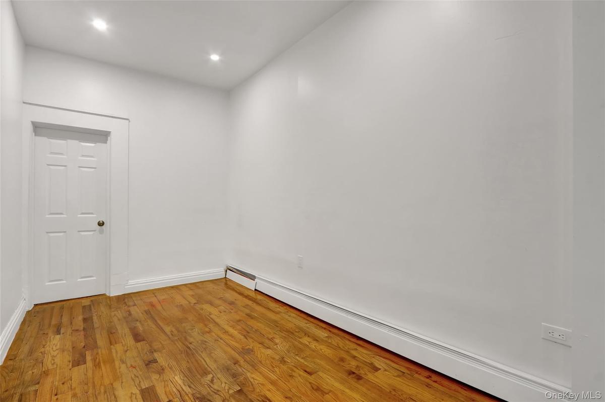 Room featuring wood-finish flooring, white walls, recessed lighting, and a white paneled door with a brass-toned knob