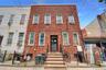 Three-story brick facade property featuring multiple windows with security bars, a ground-level entryway with a dark door, and exterior stairs with bl