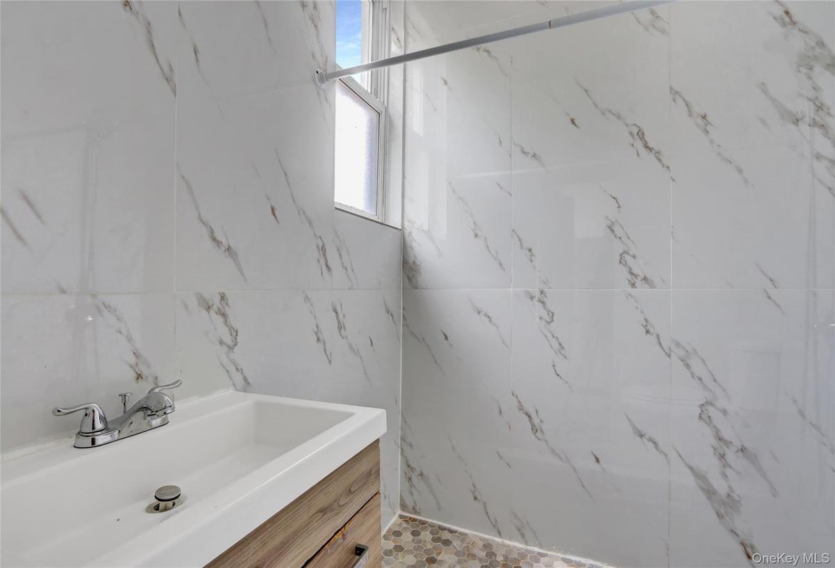 Bathroom featuring white marbled wall tiles, a window, a vanity with a white rectangular sink, a chrome faucet, and wood-finish cabinetry