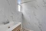 Bathroom featuring white marbled wall tiles, a window, a vanity with a white rectangular sink, a chrome faucet, and wood-finish cabinetry