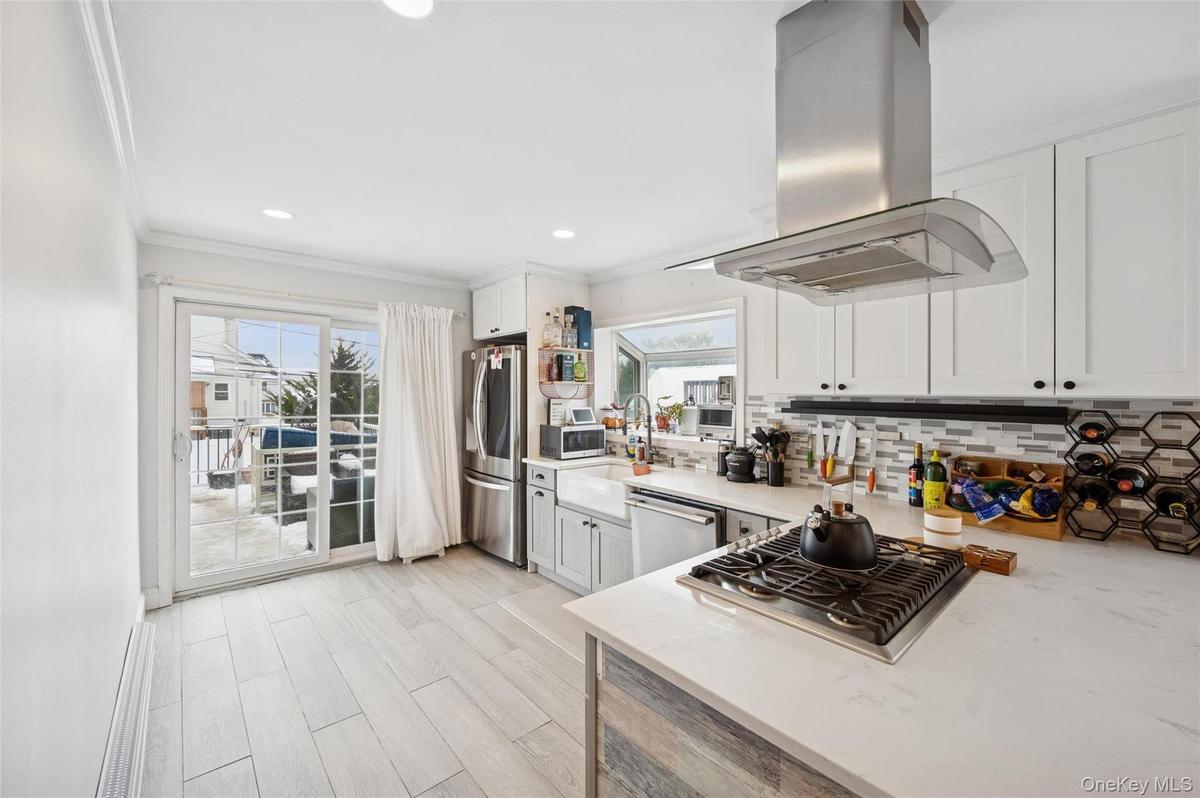 Kitchen featuring island range hood, light stone counters, appliances with stainless steel finishes, ornamental molding, and plenty of natural light
