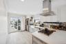 Kitchen featuring island range hood, light stone counters, appliances with stainless steel finishes, ornamental molding, and plenty of natural light